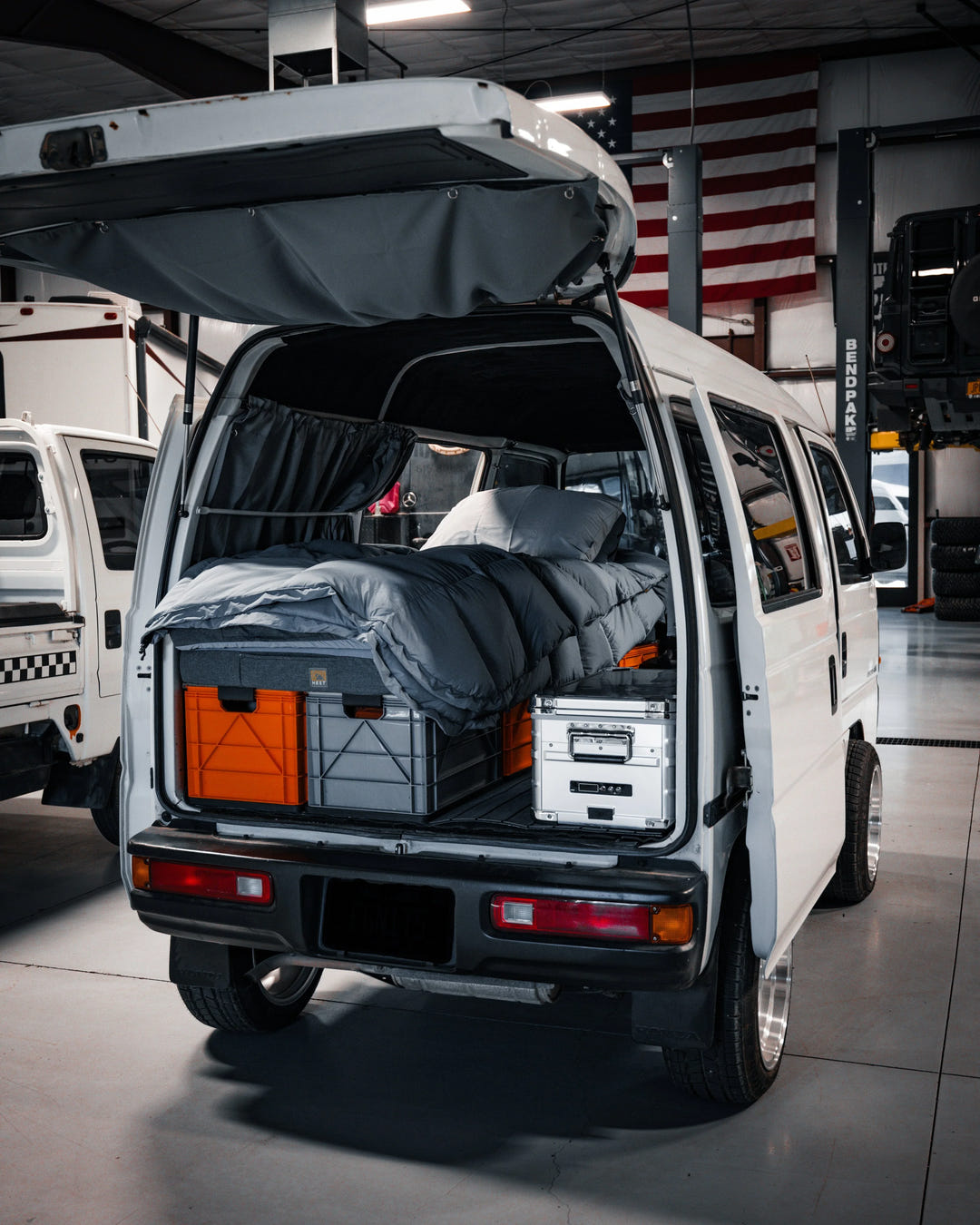 Gray SidioCrate storage system with orange bins and bedding inside a white camper van.