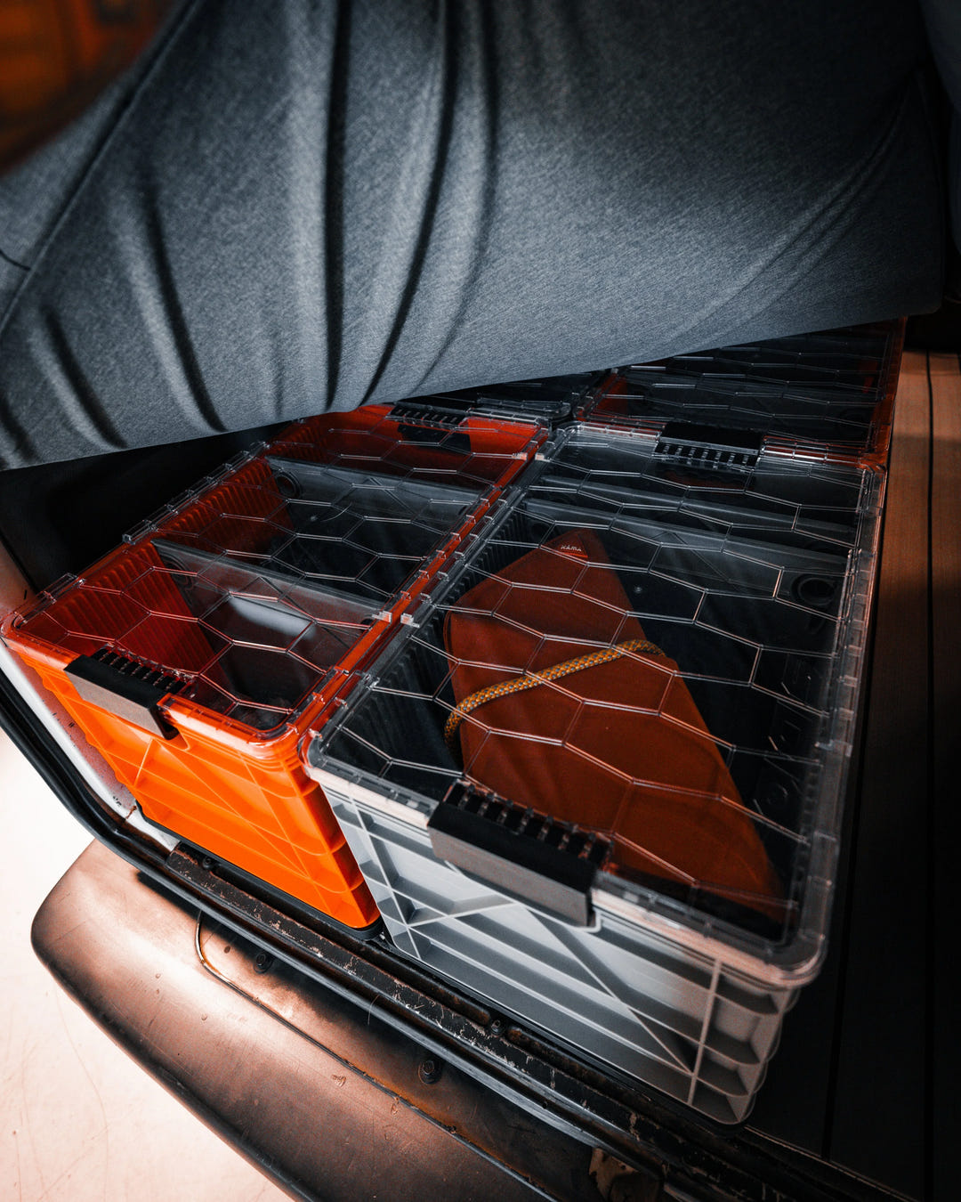SidioCrate clear plastic storage bins with orange accents inside a camper van compartment.