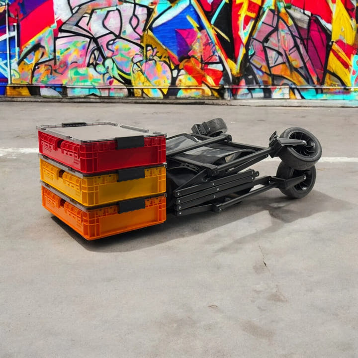 Stacked red, yellow, and orange SidioCrate collapsible storage bins with a black folding dolly cart.