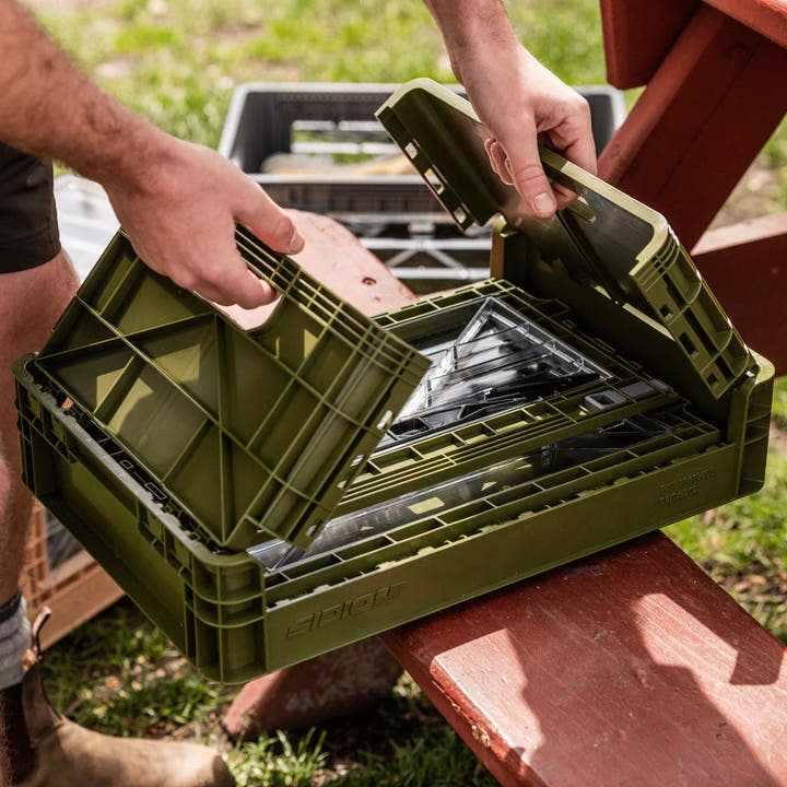 A person opens a green SidioCrate collapsible storage container on a wooden table.